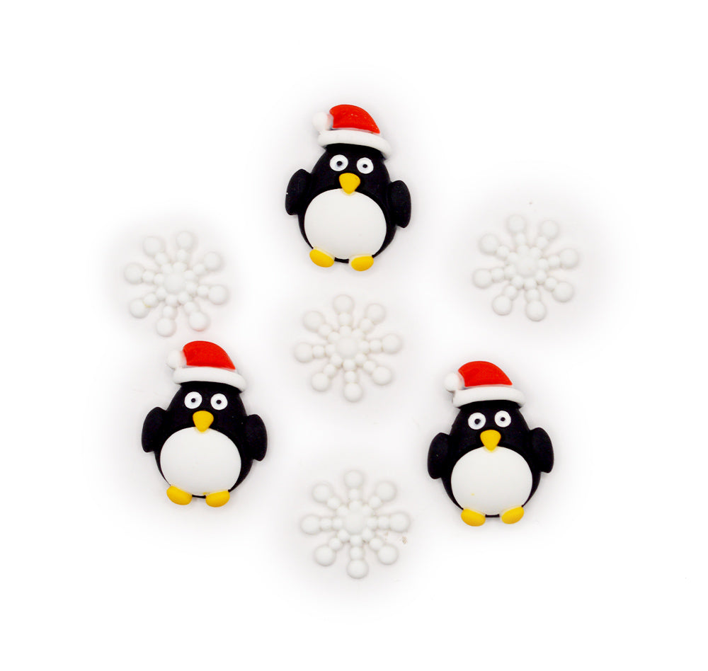 Three penguin figurines wearing Santa hats on a white background with snowflake decorations.