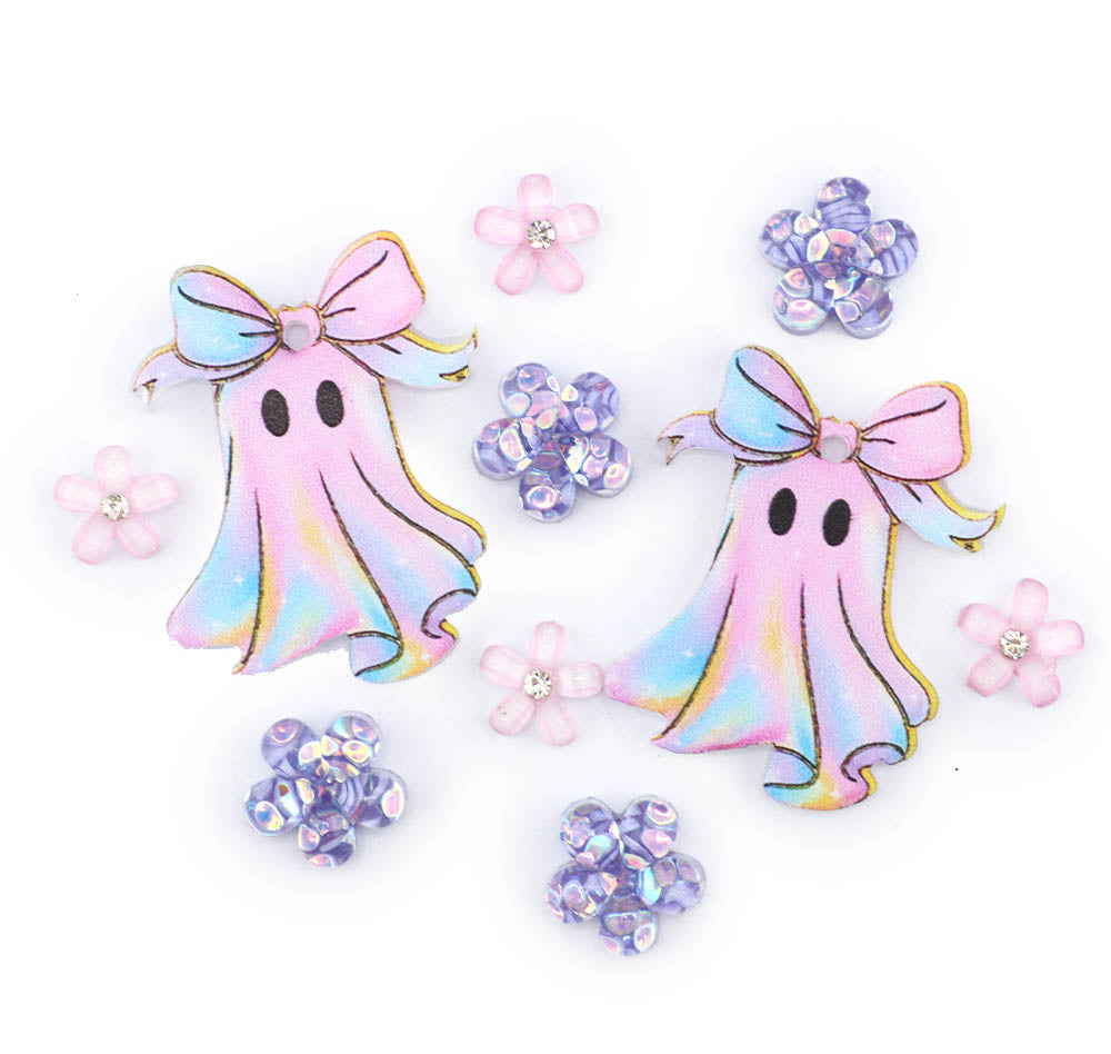 Two pastel iridescent ghost charms with pink bows and black eyes, surrounded by small pink and purple flower beads on a white background.