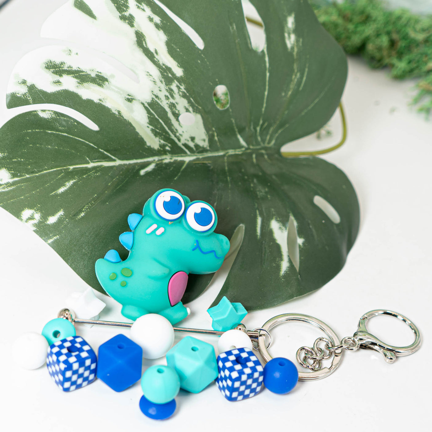 This fun DIY set includes a beadable keychain base, a large teal silicone dinosaur, and a mix of round, square, and shaped matching silicone beads