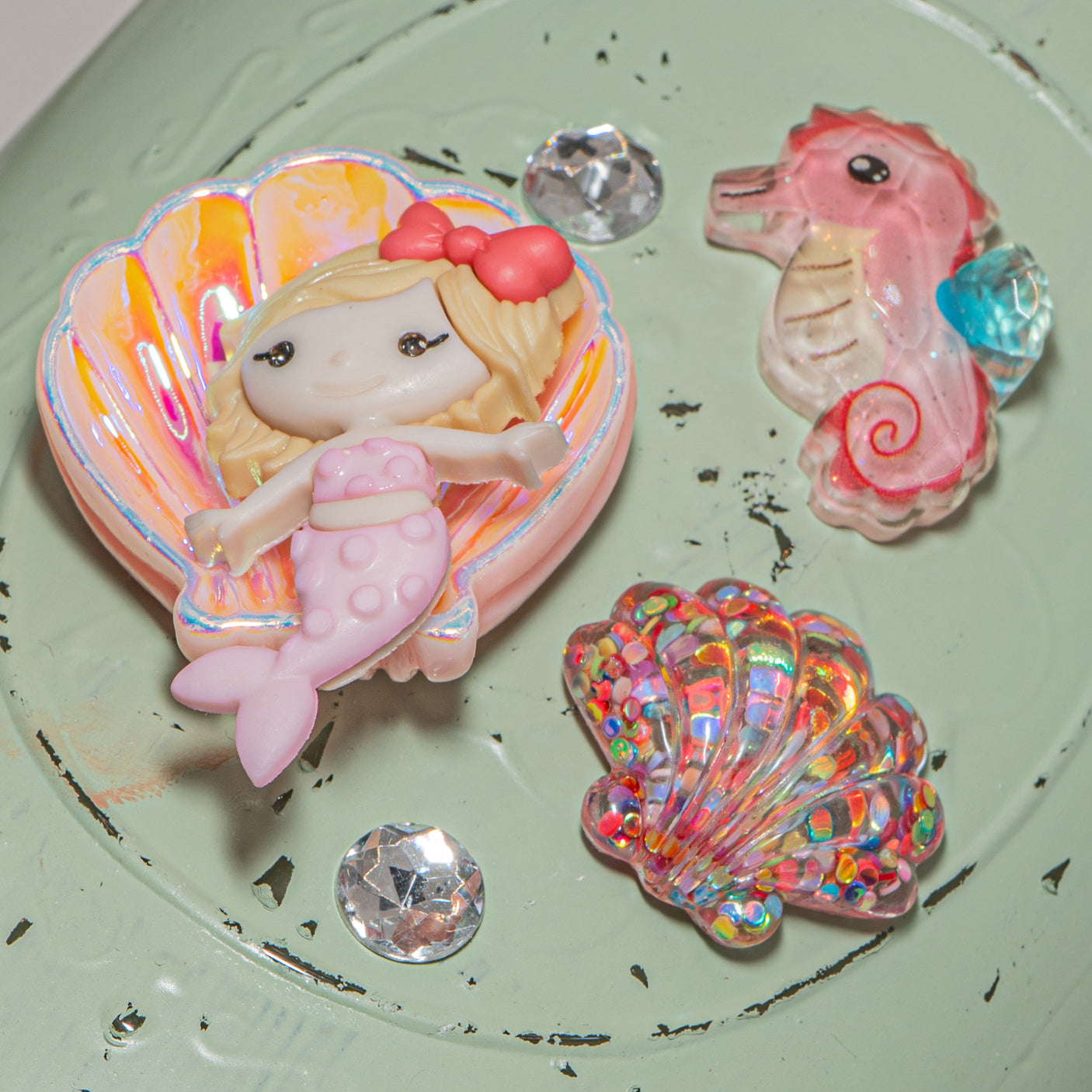 Set of decorative items including a mermaid, shell, a seahorse, and a colorful shell on a textured surface.