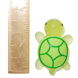 A small translucent turtle figurine in pale yellow-green with a darker green shell pattern, shown next to a metal ruler for scale on a white background.