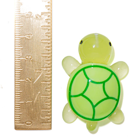 A small translucent turtle figurine in pale yellow-green with a darker green shell pattern, shown next to a metal ruler for scale on a white background.