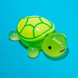 A translucent green and yellow turtle toy with a smiling face, photographed on a solid bright blue background.