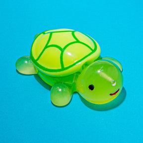 A translucent green and yellow turtle toy with a smiling face, photographed on a solid bright blue background.