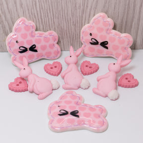 Pink bunnies craft embellishments and sew thru hearts on a wood background