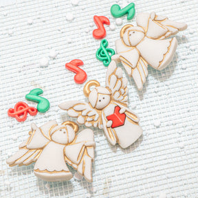 Craft buttons shaped like angels with musical notes on a textured white surface
