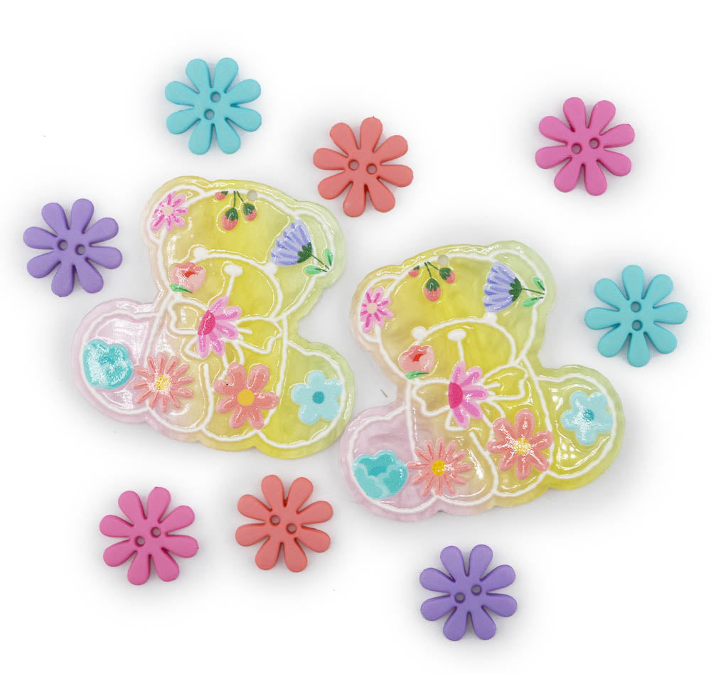 Two translucent yellow teddy bear-shaped charms decorated with colorful pressed flowers, surrounded by matching loose flower-shaped buttons on a white background.