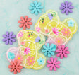 Two translucent yellow cloud-shaped resin charms decorated with colorful flowers and hearts, surrounded by matching flatback buttons on a light blue textured background.