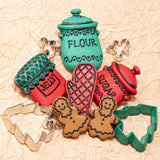 Set of plastic button jars labeled 'Flour', 'Jelly', 'Sugar' with corresponding cookie cutters on a textured beige background.