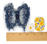 A handmade denim butterfly patch in blue and white, shown next to a wooden ruler, a small white daisy, and a yellow and blue floral patch on a white background.