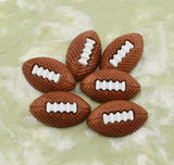 Six brown football-shaped craft buttons with white laces, arranged on a light green marbled surface.
