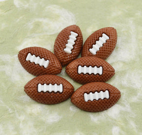 Six brown football-shaped craft buttons with white laces, arranged on a light green marbled surface.