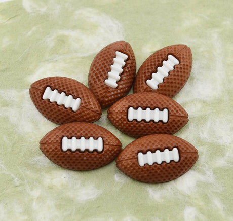 Six brown football-shaped craft buttons with white laces, arranged on a light green marbled surface.