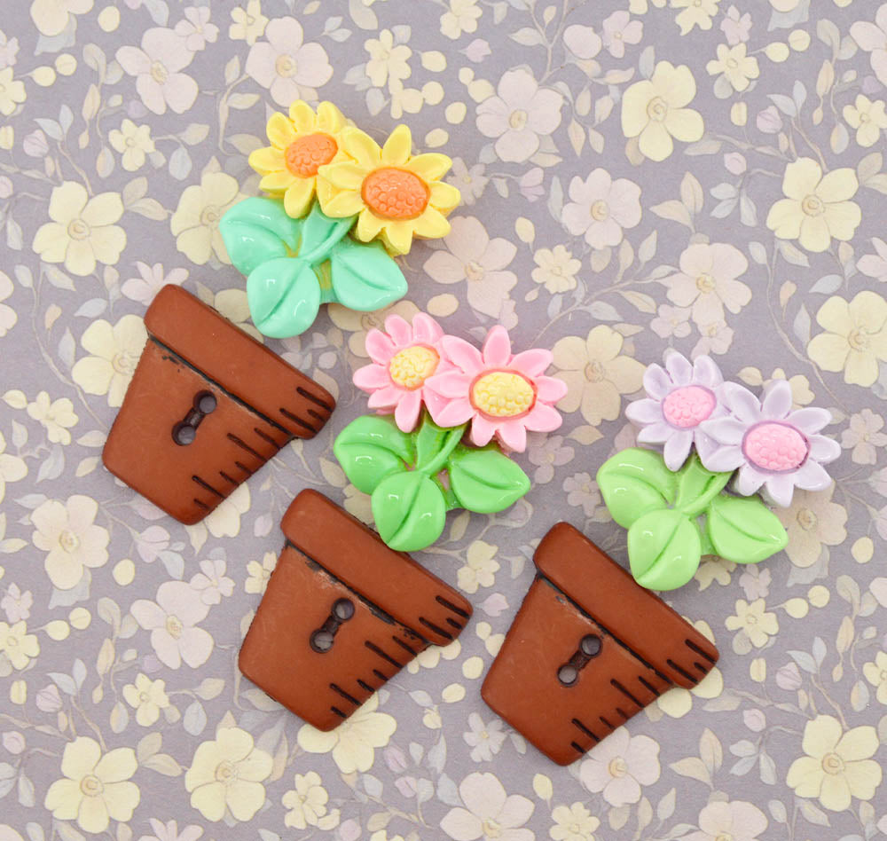 Three clay pot sewing buttons and three resin flower embellishments on a purple floral background