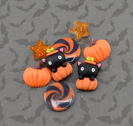 A set of Halloween-themed polymer clay charms and buttons featuring black cats in witch hats, orange pumpkins, a glittery orange star, and orange-and-black swirl designs, displayed on a gray background with a subtle bat pattern.