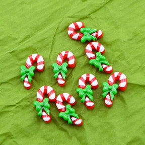 Six small candy cane-shaped craft charms with green holly accents, arranged on a textured green background.