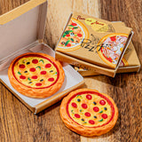 Two round, pizza-shaped items displayed on a wooden surface, with one inside an open cardboard box and one outside. The packaging is printed with pizza illustrations and the word "Pizza.