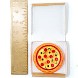 A miniature toy pizza in a small white and brown cardboard box, shown next to a brass ruler for scale on a white background.