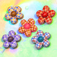 Five handmade flower-shaped craft embellishments with plaid and patterned petals, arranged on a colorful pastel background.