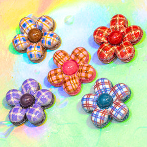Five handmade flower-shaped craft embellishments with plaid and patterned petals, arranged on a colorful pastel background.