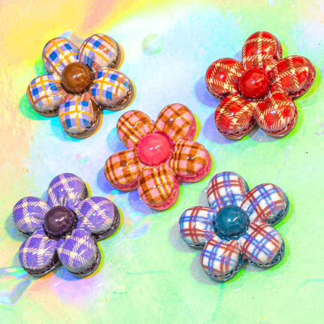 Five handmade flower-shaped craft embellishments with plaid and patterned petals, arranged on a colorful pastel background.