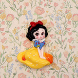 A glossy Snow White resin craft embellishments set against a floral wallpaper background.