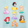Seven small cartoon princess craft embellishments arranged on a light aqua background. The characters include Snow White, Cinderella, Rapunzel, Ariel, Belle, and Jasmine, each shown in a different colorful dress.