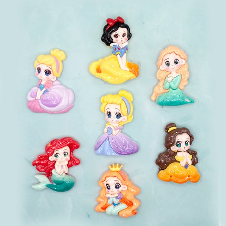 Seven small cartoon princess craft embellishments arranged on a light aqua background. The characters include Snow White, Cinderella, Rapunzel, Ariel, Belle, and Jasmine, each shown in a different colorful dress.