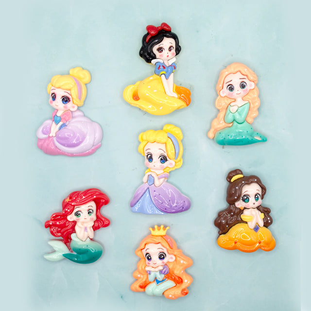 Seven small cartoon princess craft embellishments arranged on a light aqua background. The characters include Snow White, Cinderella, Rapunzel, Ariel, Belle, and Jasmine, each shown in a different colorful dress.