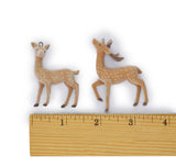 Two small deer figurines, one standing and one with antlers, shown above a wooden ruler on a white background to indicate size.