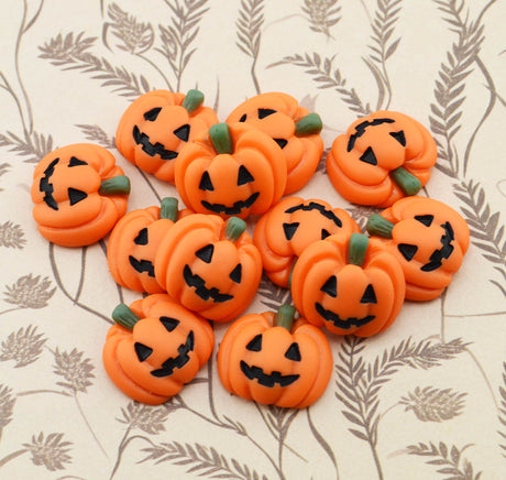 A group of small orange jack-o'-lantern pumpkins with carved black faces and green stems, arranged on a beige patterned surface.