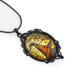 A gothic-style oval pendant necklace featuring a stained-glass design with yellow, orange, and green tones, set in a black filigree frame on a black cord.