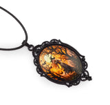A gothic-style oval pendant necklace featuring a black ornate metal frame and a glass dome insert depicting a spooky forest scene with a witch, bats, and a full moon, suspended from a black cord on a white background.