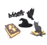 A set of black Halloween-themed decorative cutouts and paper cutouts, including a witch hat, a black cat sitting on an open book, a glowing book with ghosts, a bird, and a cursive 'Moshi' design, displayed on a white background.