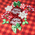 Collection of Christmas-themed embellishments including candy canes, holly leaves, and 'Merry Christmas' ornaments on a red plaid background