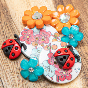 A floral and ladybug-themed embellishment pack full of vibrant orange and blue accents on a wood background