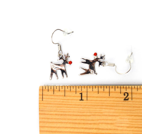 A pair of silver-toned dangle earrings shaped like stylized reindeer with small red accents, shown above a wooden ruler on a white background for scale.