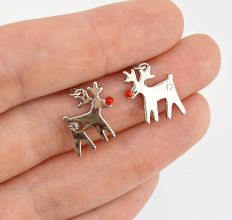 Two small silver reindeer charms with red nose accents resting on a person's fingers against a white background.