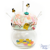 Sewing embellishments and cute bees are used to dress up a pin cushion
